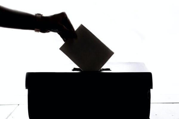 A silhouette of a hand dropping a ballot in a ballot box is pictured.