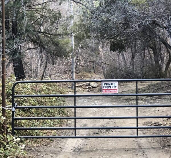 locked gate with a no trespassing sign across dirt road