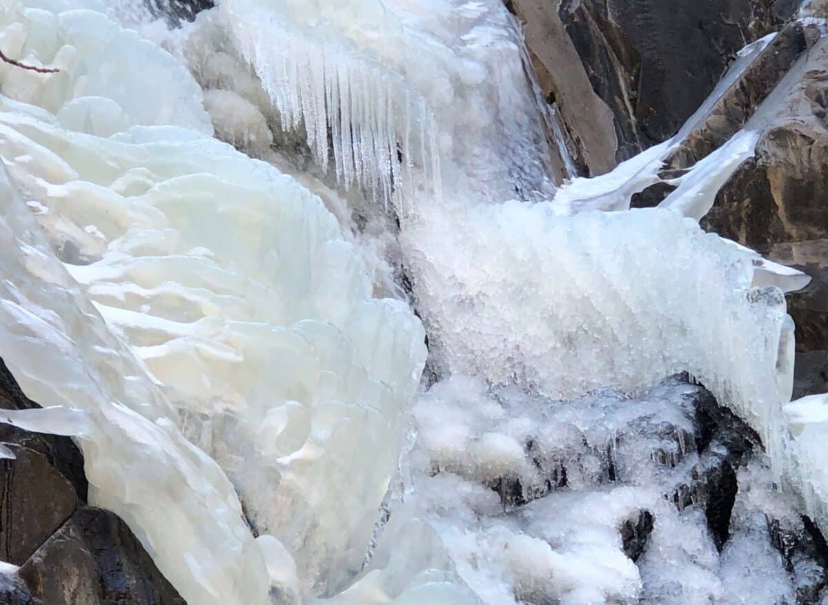 partially frozen waterfall with ice bubbles, stalactites ,snow and rushing water.