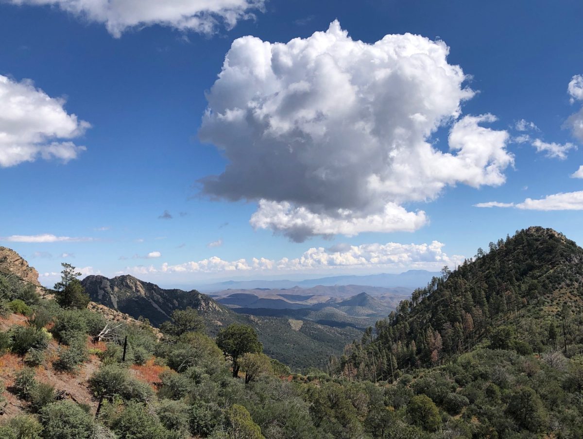 Long view facing east goes all the way to Caballo Mountains. A fluffy white cloud floats in a dark blue sky.