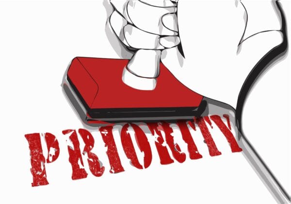 A pictured hand holds a rubber stamp over a document marked with the word priority.